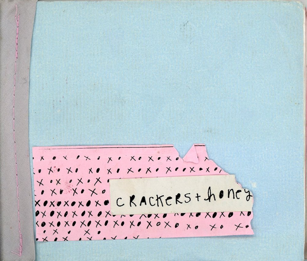 A handmade zine cover with a blue background, hand stitching and a small handwritten title saying Crackers + Honey
