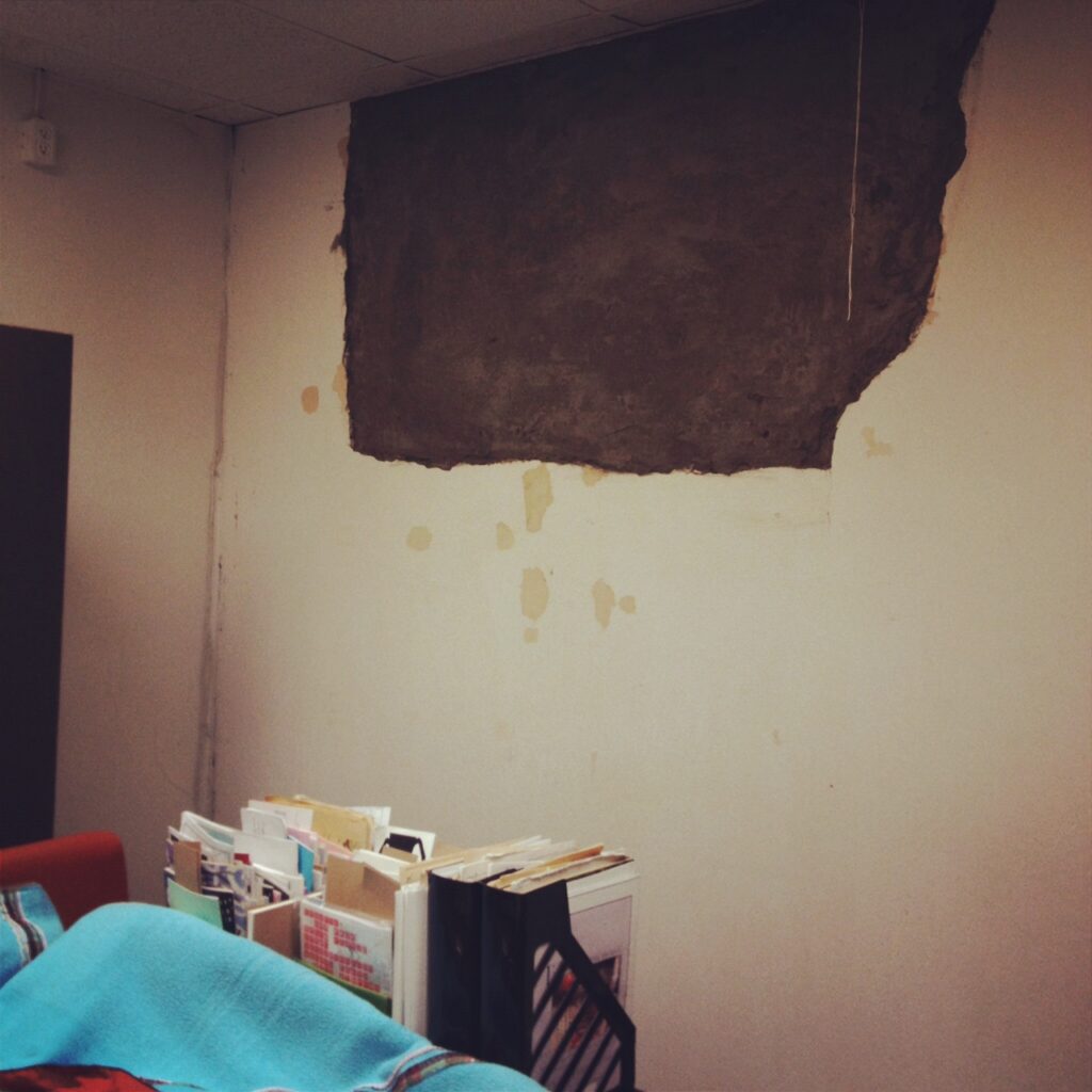 Wall of the TZL space. Signs of water damage covering most of the wall. Wall is also discoloured, brown water damaged over the white walls
